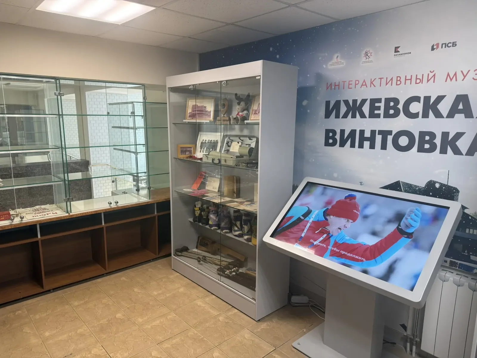 Сенсорный стол у витрины с памятными сувенирами: на экране спортсменка