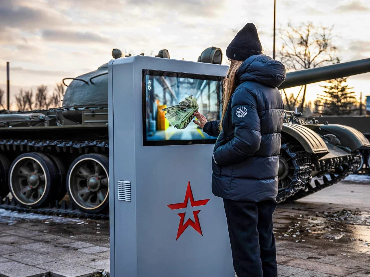 Посетительница у сенсорного терминала рядом с экспонатом бронетехники в парке «Патриот»